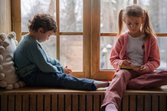 A boy and a girl sitting on a windowsill; the girl is playing with a toy.