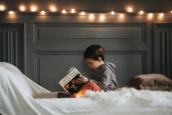 A boy sitting in bed, reading a book.